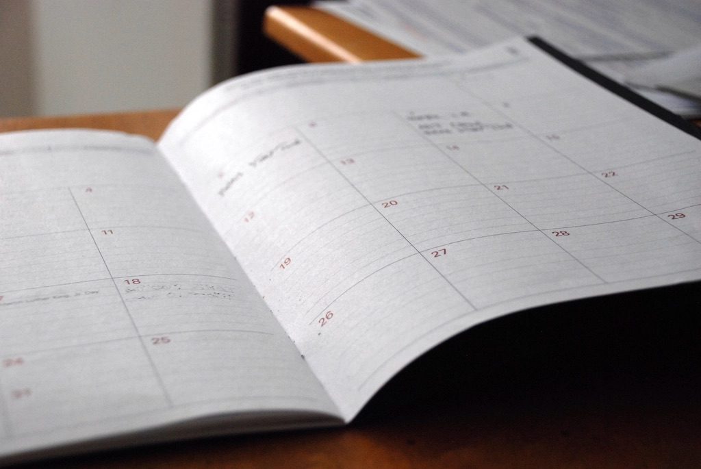A desk calendar and clock beside a task list, marking time tracked on daily work